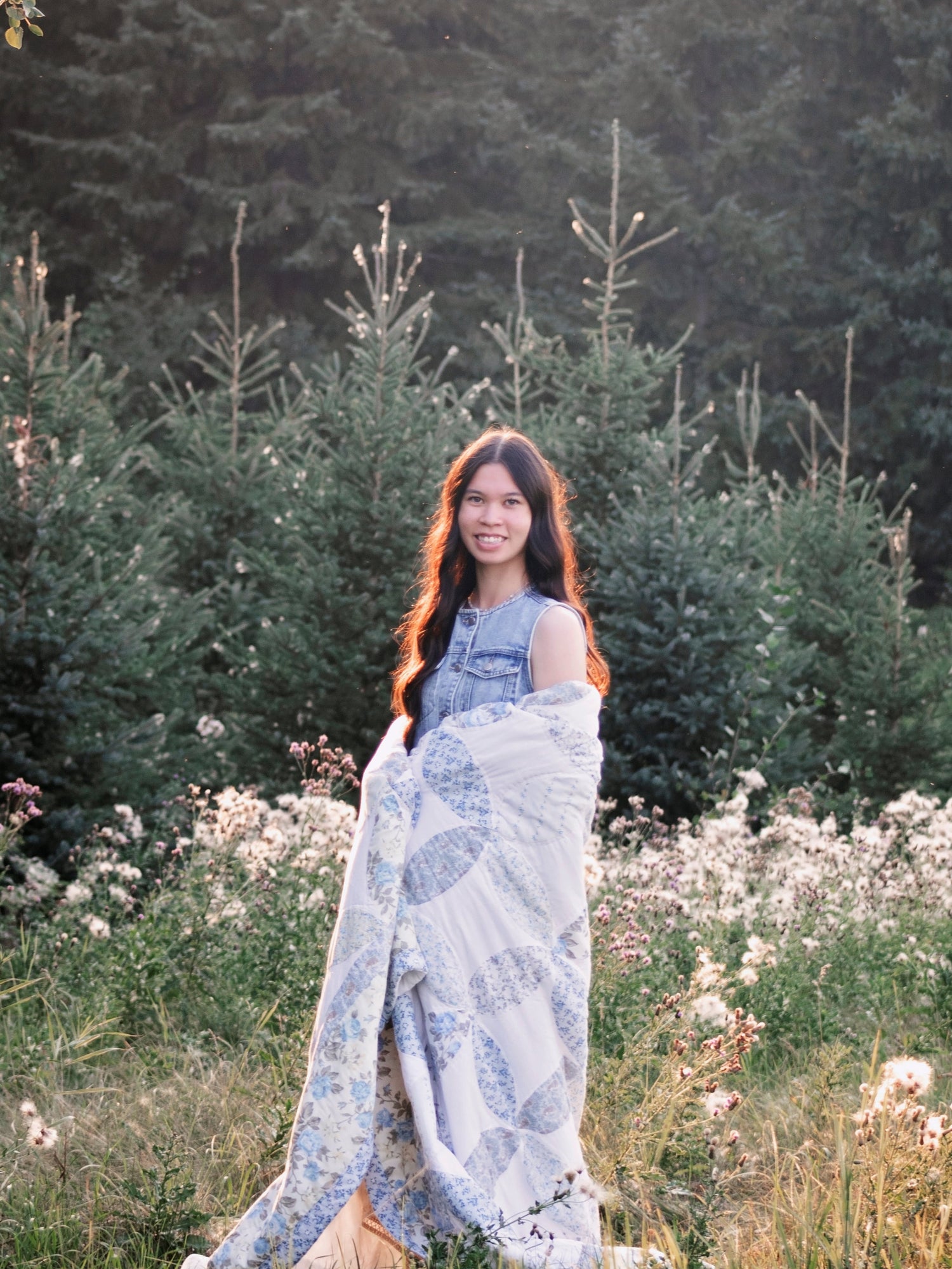 Woman wrapped in a quilt standing in a field with trees in the background